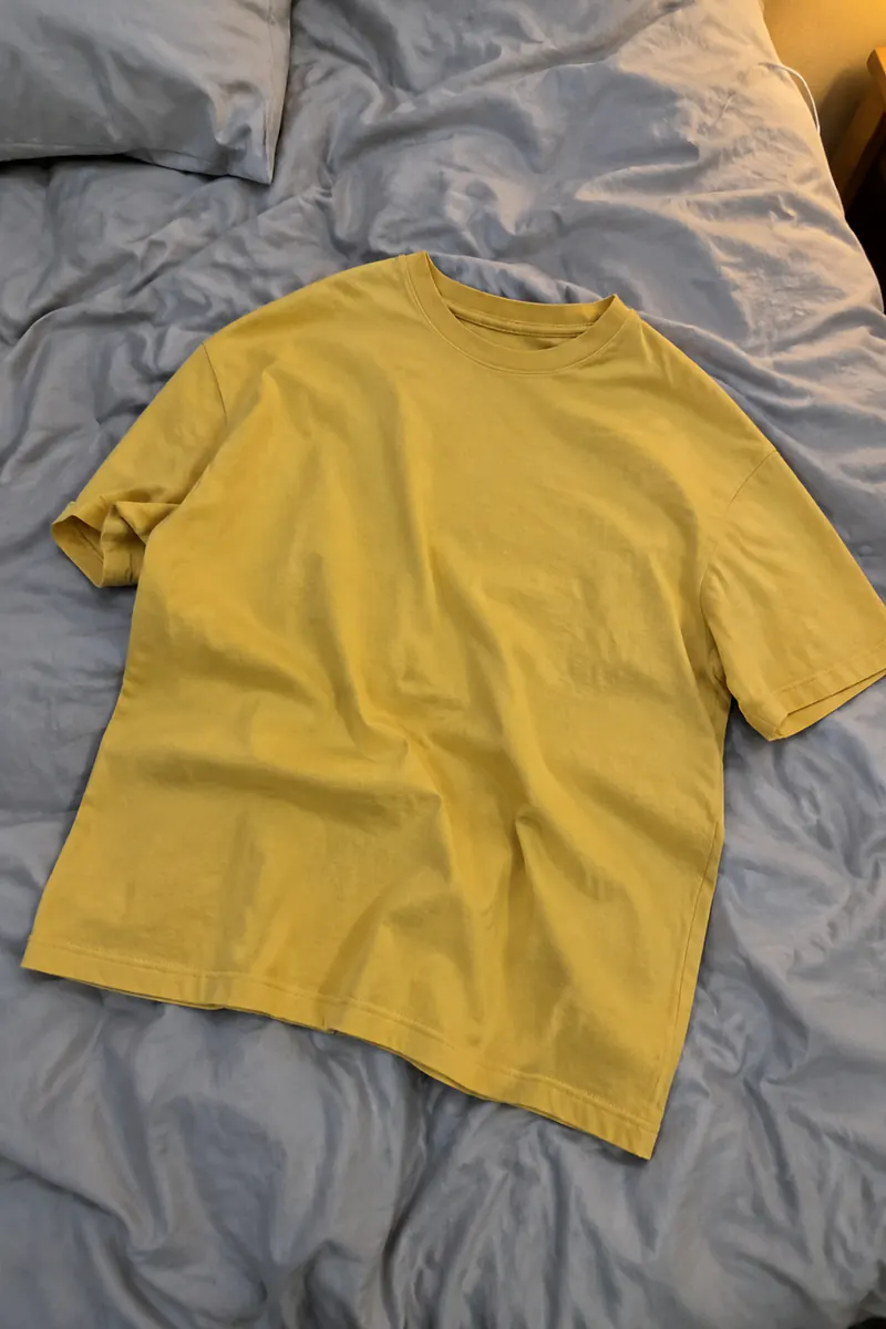 Telefoonfoto van een geel T-shirt op een verfrommeld bed